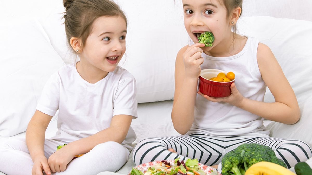 Healthy food at home. Happy two cute children eating fruits and vegetables in the bedroom on the bed. Healthy food for children and teenagers.