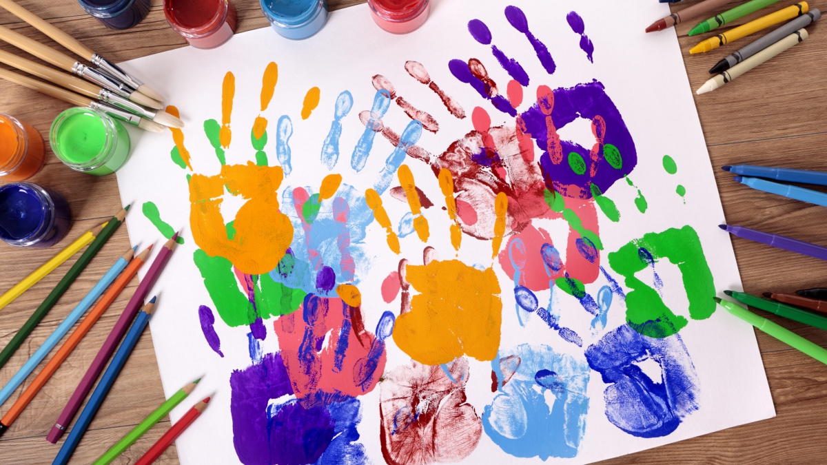 Painted handprints with art and craft equipment on a school table.