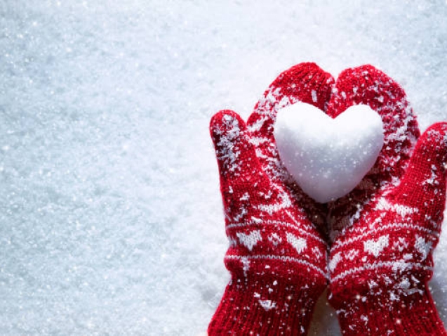 Female hands in knitted mittens with snowy heart against snow background. Love, winter and Valentines day romantic creative concept with copy space for text